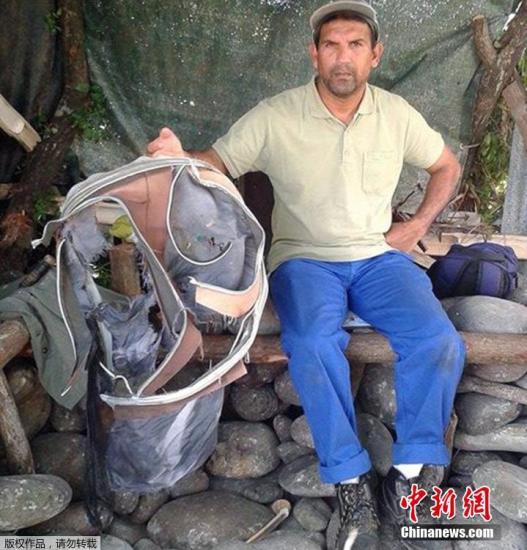 圖為當?shù)貢r間7月30日，留尼旺島上的一名海岸清潔人員展示他找到的一個手提箱的殘骸。